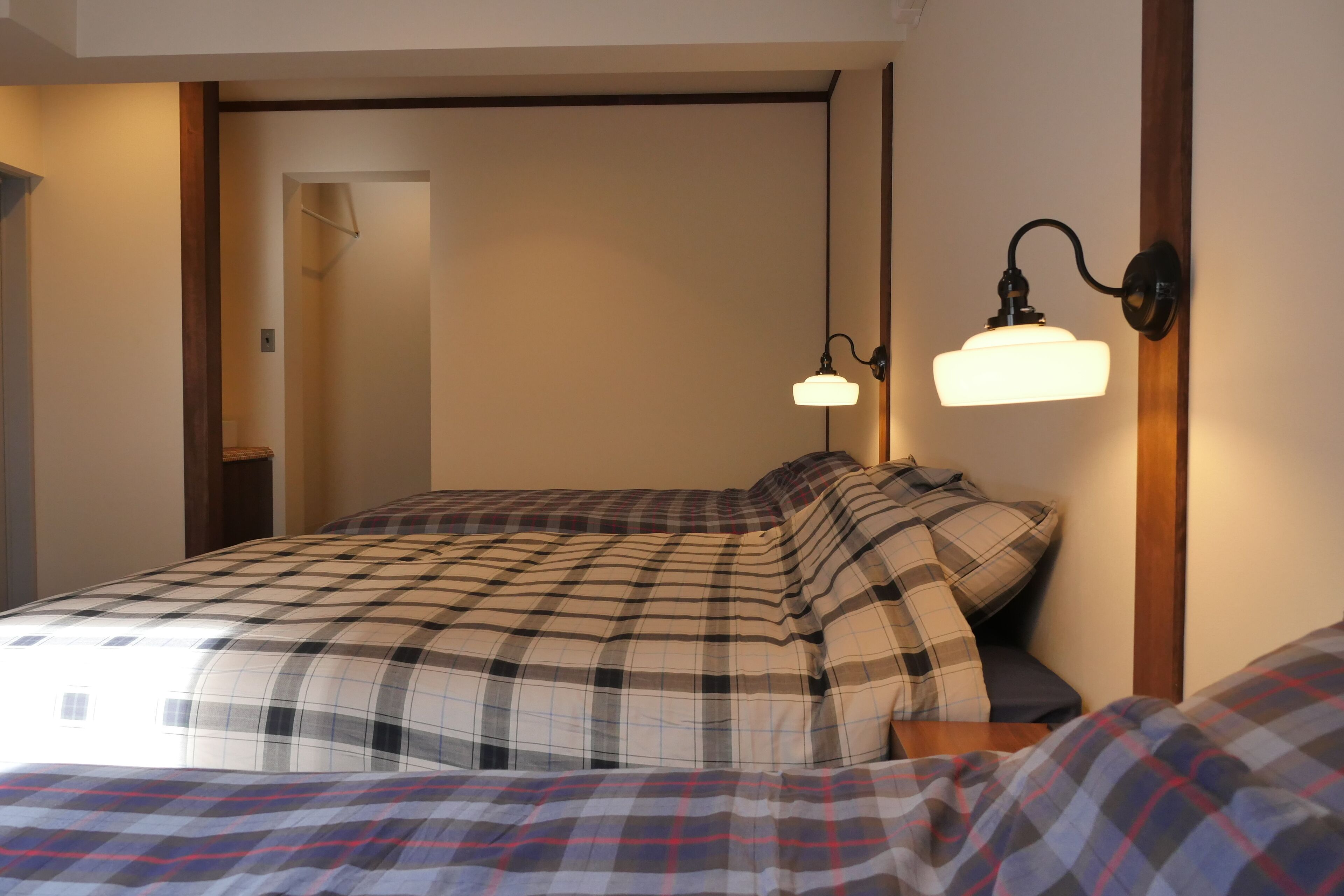 A bedroom with a bed, a nightstand, a wall-mounted lamp, and a door leading to another room.