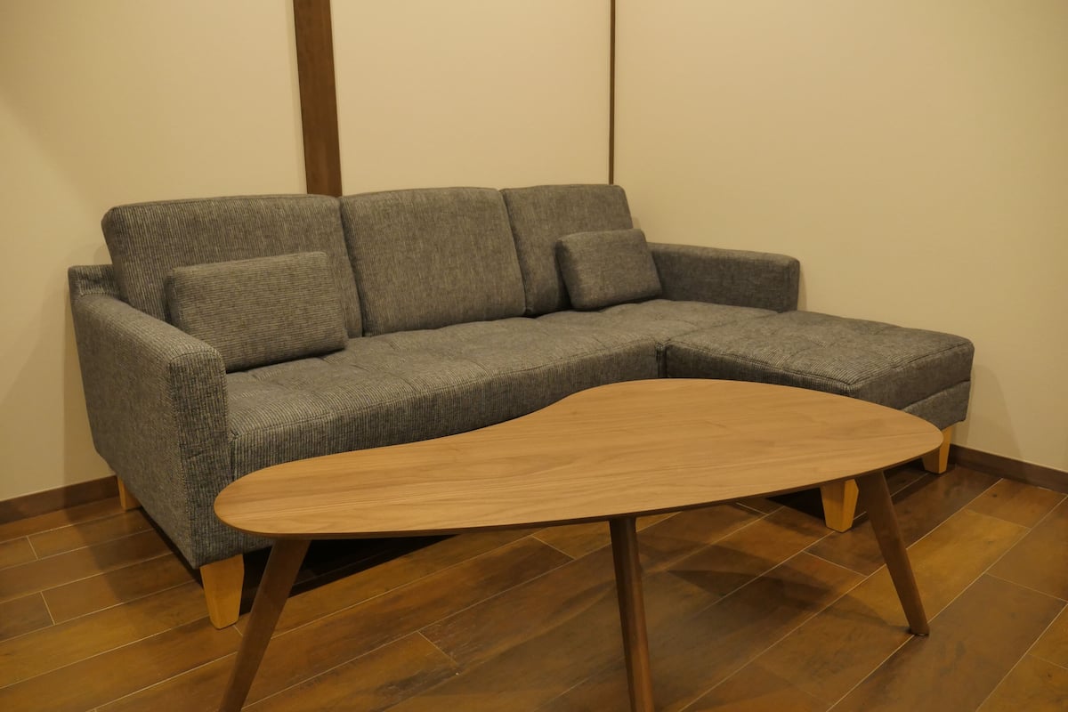 Um sofá modular cinzento com pés de madeira e uma mesa de centro de madeira à frente.