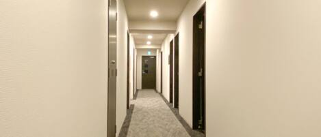 A hotel hallway with carpeted floors, doors on both sides, and a ceiling light.