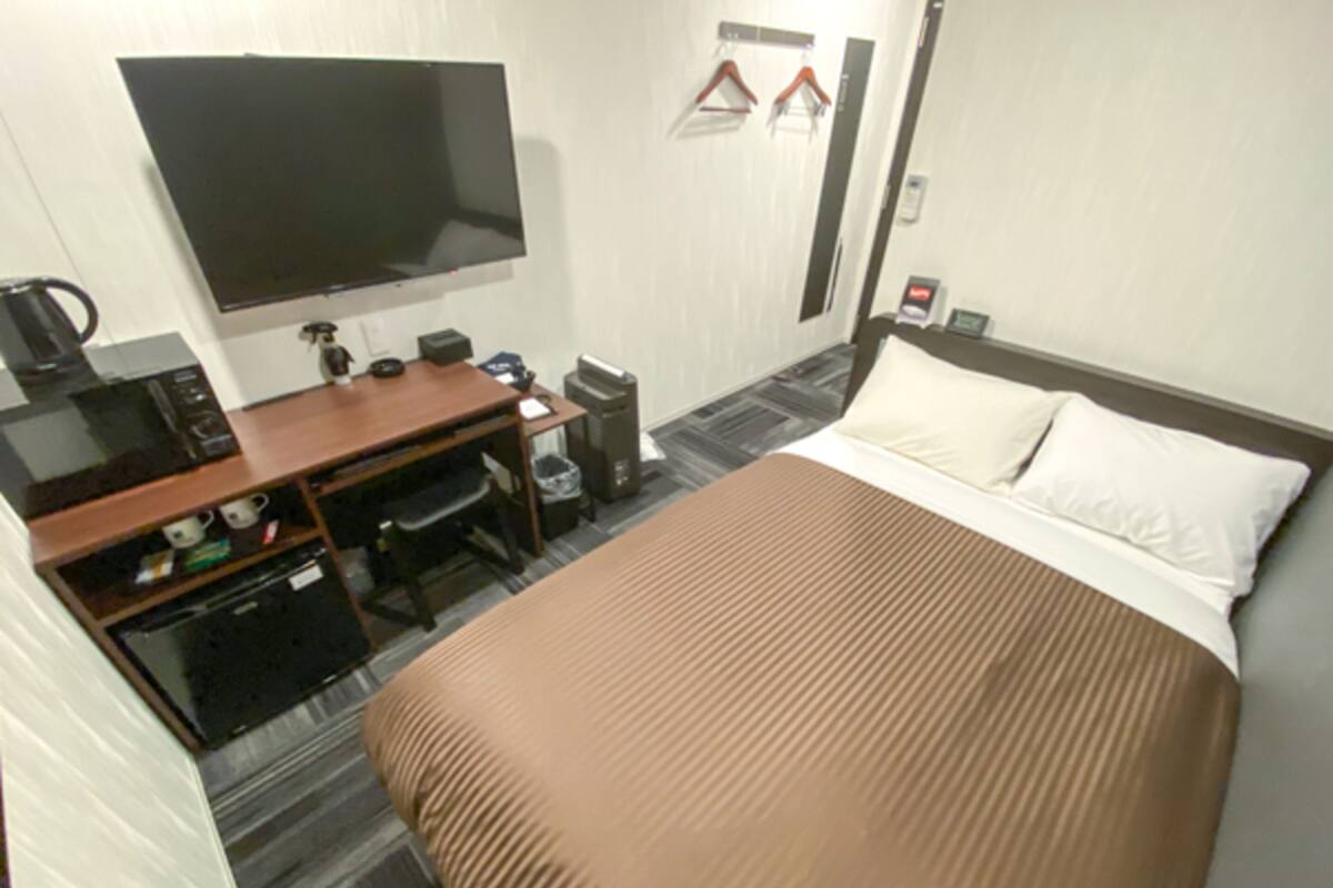 Habitació d'hotel amb llit, escriptori amb ordinador, televisió i cafetera.