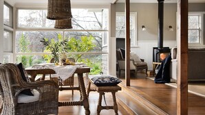 Un salon chaleureux avec une grande fenêtre, des meubles en osier, une cheminée et une vue sur la verdure environnante.