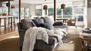 Un salon chaleureux avec un canapé gris agrémenté de différents coussins et d’un plaid blanc tricoté.
