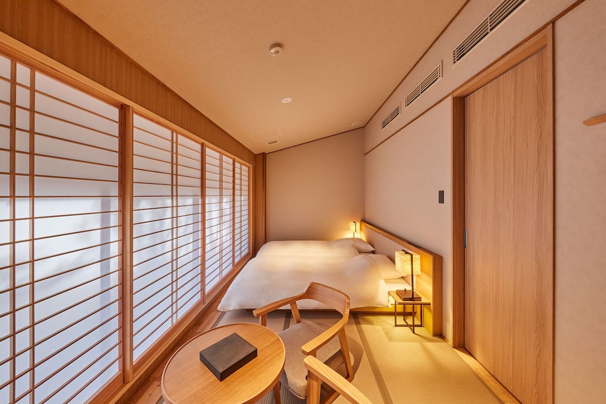 Ein traditioneller japanischer Raum mit Tatami-Boden, einem niedrigen Bett, einem Holztisch und einem verschiebbaren Shoji-Bildschirm.