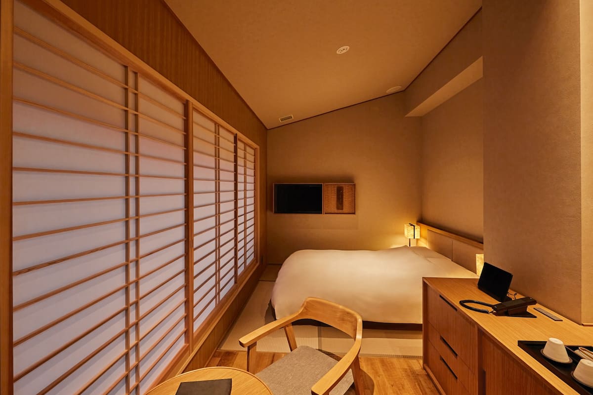 Ein Hotelzimmer mit einem Bett, einem Schreibtisch mit Computer, einem Stuhl und einer verschiebbaren Shoji-Schirmwand.