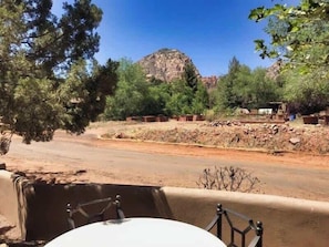 Mesa e cadeiras em área externa arborizada com vista para uma colina rochosa e árvores.