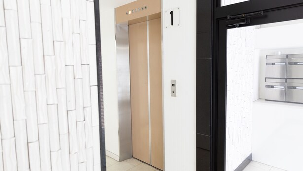 An elevator with a beige interior, a white wall with a geometric pattern, and a door with the number 1. - SUNDAY peace room Tokaichi203 (Hiroshima)