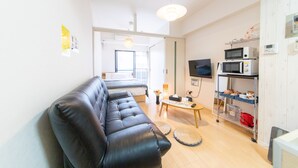 A modern living room with a black leather sofa, a wooden coffee table, a TV, and a kitchenette with a microwave and toaster. - SUNDAY peace room Tokaichi203 (Hiroshima)