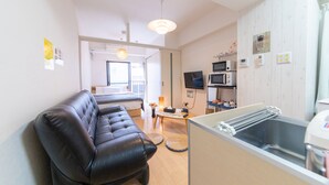A modern living room with a leather sofa, a dining area with a table and chairs, a kitchen with appliances, and a large window. - SUNDAY peace room Tokaichi203 (Hiroshima)