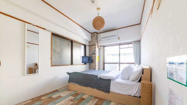A bedroom with a wooden bed, a television, a window with curtains, and a wall-mounted air conditioner. - SUNDAY peace room Honkawa II (Hiroshima)
