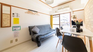 A modern room with a sofa, a dining table, and a TV. There are signs on the wall and a window with curtains. - SUNDAY peace room Honkawa II (Hiroshima)