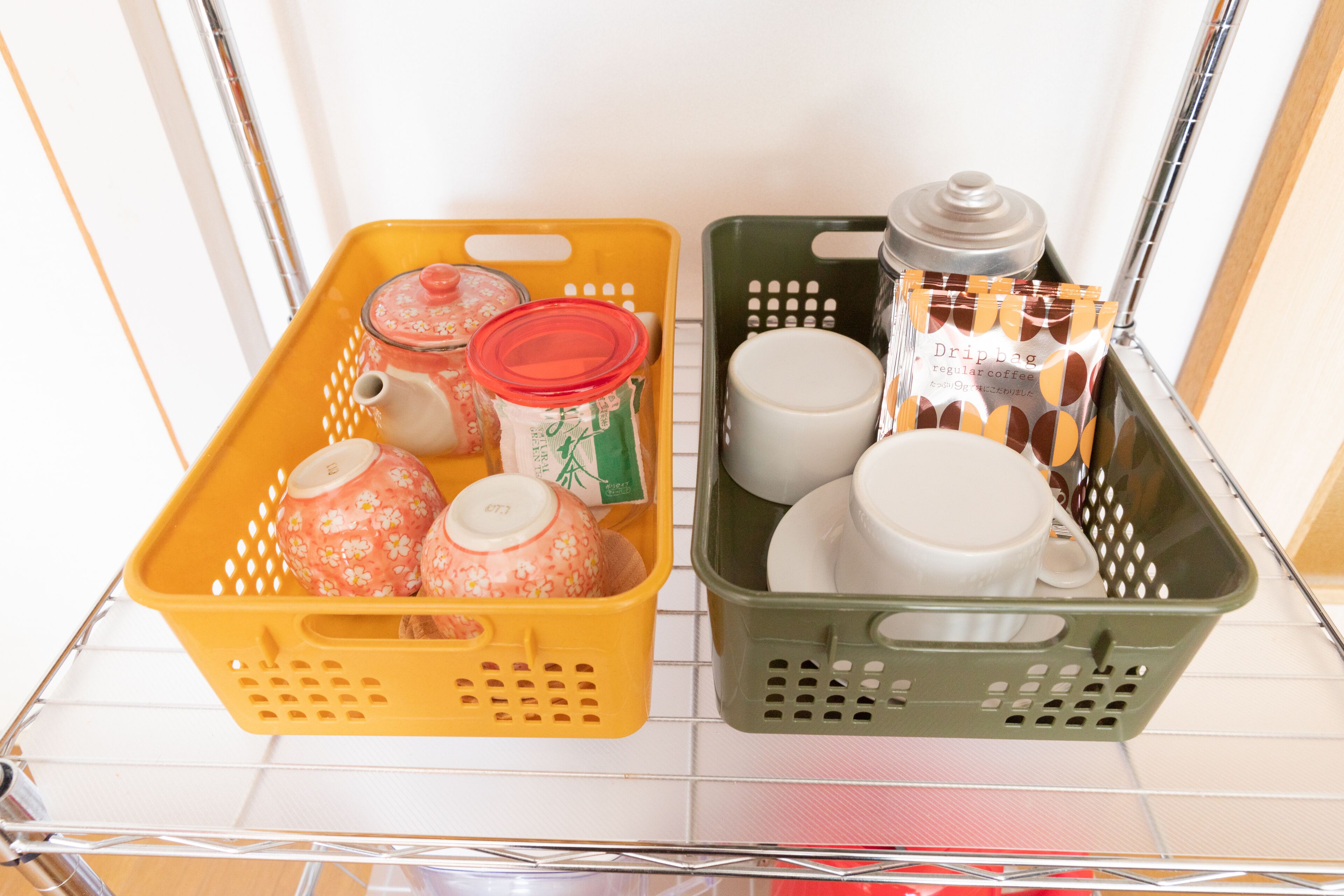 Two baskets on a shelf, one yellow and one green, containing kitchen items like jars and cups.