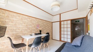 A modern room with a brick wall, a white table with black chairs, a grey sofa, and a traditional sliding door. - SUNDAY peace room Honkawa II (Hiroshima)