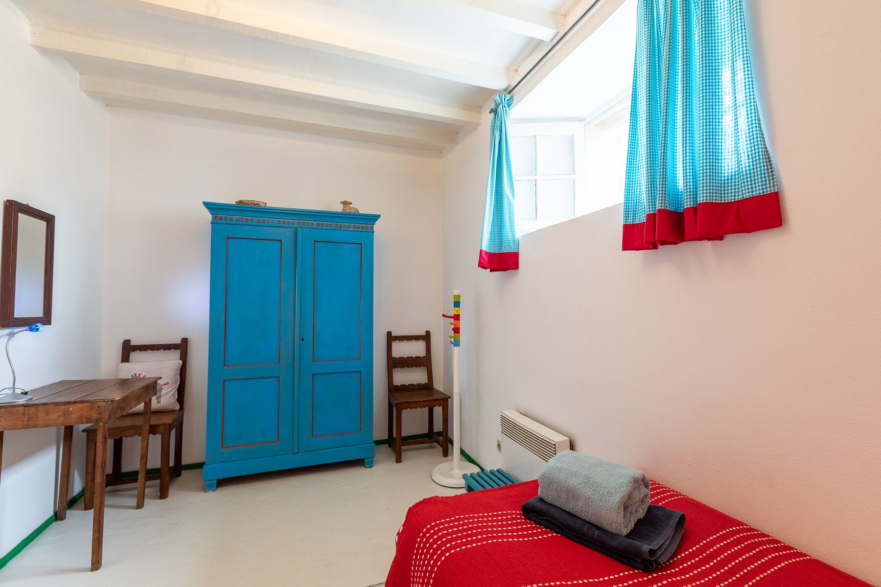 Un dormitorio con una cama, un escritorio de madera, un armario azul y una ventana con cortinas.