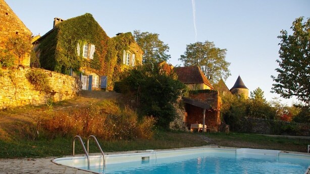 A stone building with a swimming pool, surrounded by greenery and trees.