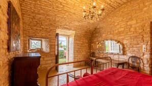 A rustic room with exposed brick walls, a wooden bed, a metal railing, a chandelier, and a window with a view of greenery.