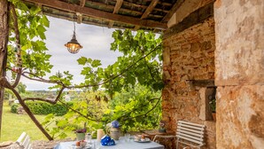 A rustic outdoor dining area with a table set for two, a bench, and a view of a vineyard.