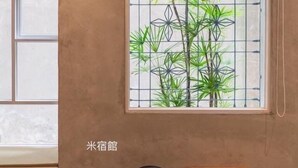 Quarto com janela, apresentando uma planta de bambu, luminária na parede, ventilador e um armário de madeira.