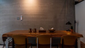 Uma área de refeições com uma mesa de madeira, três cadeiras, uma pequena planta em vaso, um abajur e uma caixa de lenços.