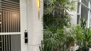 Fachada de edifício com parede texturizada, portão de metal e vasos de plantas.