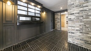 A modern kitchen with dark cabinetry, a black tiled floor, and a brick accent wall. - Hotel Chicago (Changwon)