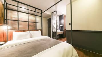 A hotel room with a bed, a nightstand, a mirror, and a bathroom with a sink and mirror.