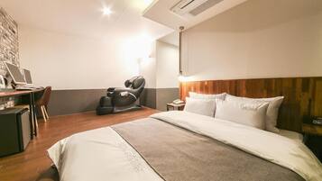 Habitación de hotel con cama, sillón de masaje, escritorio con laptop y una kitchenette pequeña.