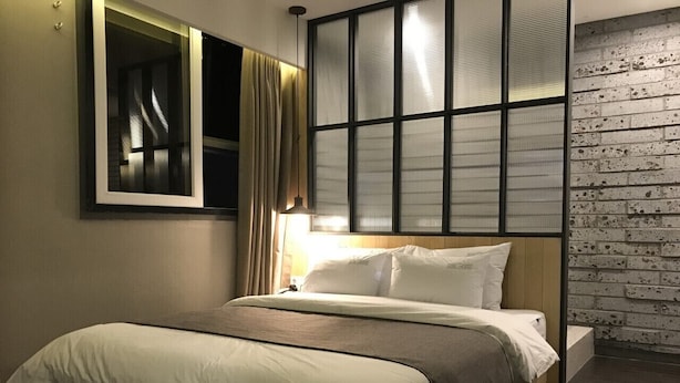 A bed with a wooden frame, a headboard with a window, and a brick wall. - Hotel Chicago (Changwon)