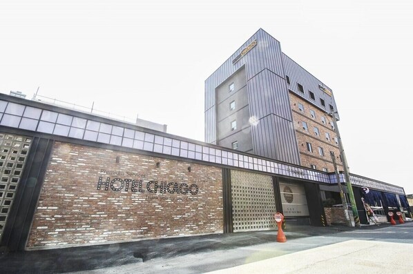 A hotel with a modern facade, a prominent sign for HOTEL CHICAGO, and a brick wall with a window pattern. - Hotel Chicago (Changwon)