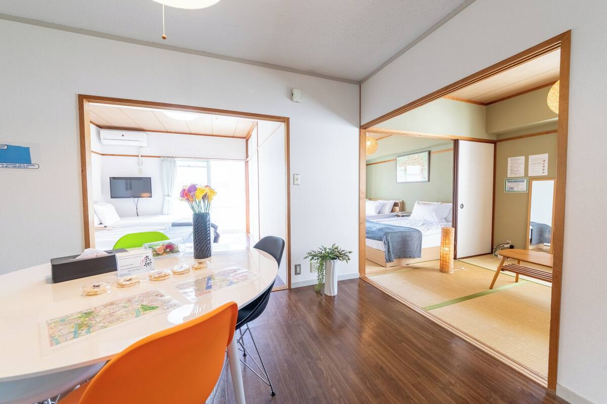 Ein modernes Hotelzimmer mit Holzboden, einem Essbereich mit Tisch und Stühlen sowie einem Bett mit Nachttisch.