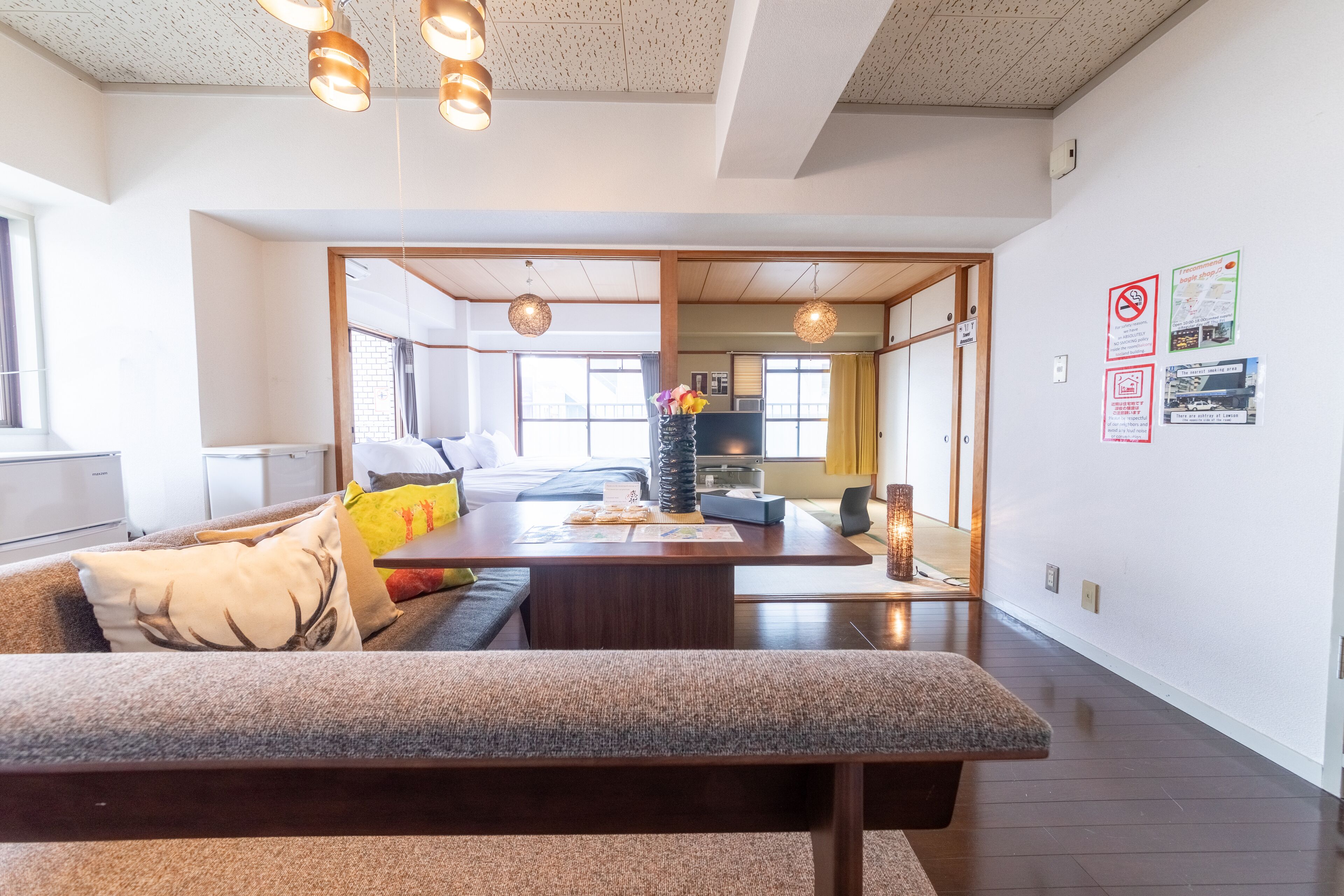 A modern living room with a sofa, a coffee table, and hanging lights. There is a kitchen area visible in the background.