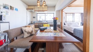 A modern living room with a wooden table, a sofa, and a bed. There is a kitchen area in the background with a window. - SUNDAY peace room Nakashima (Hiroshima)