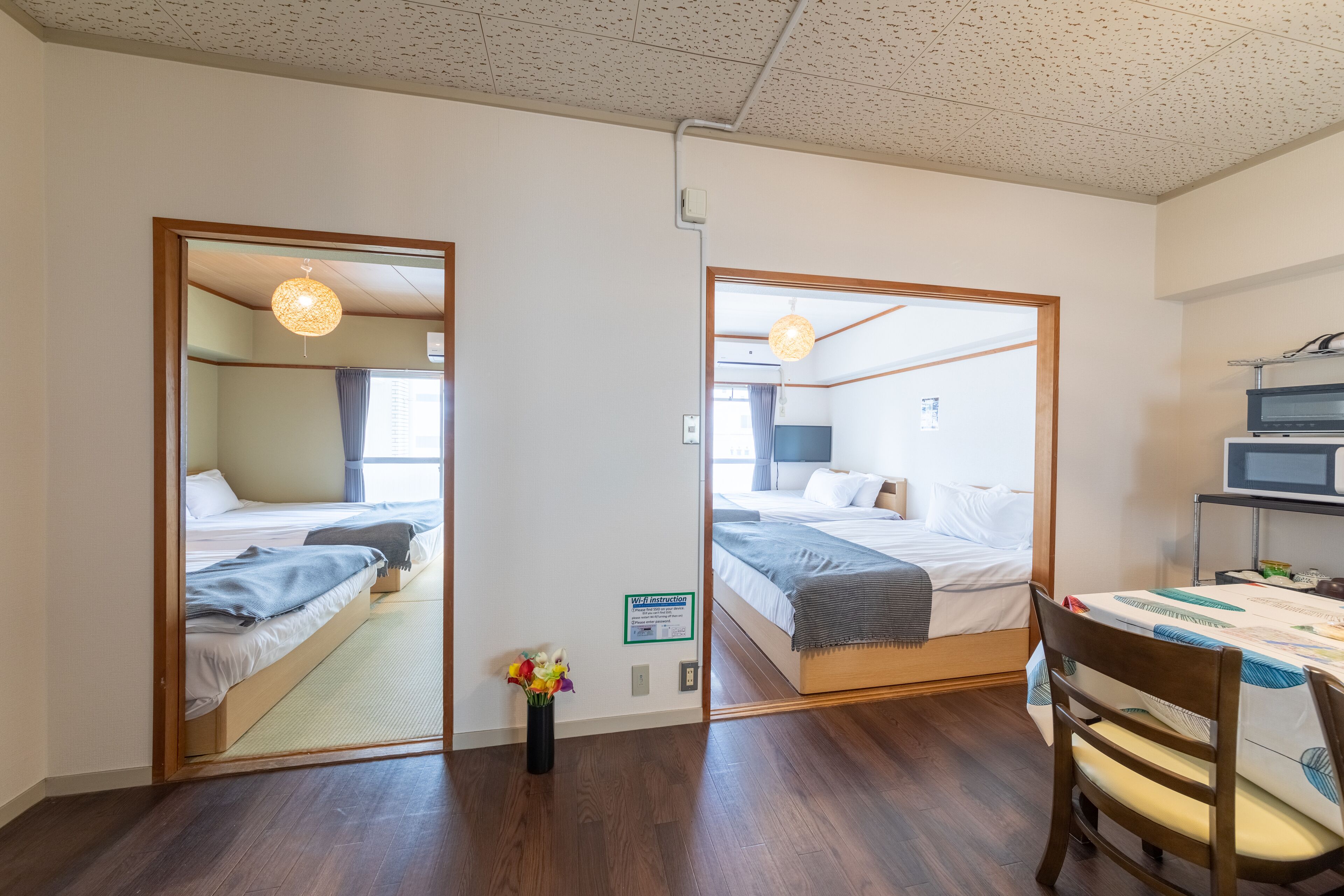 A hotel room with a wooden floor, a bed with a gray blanket, a desk with a chair, and a mirror reflecting the room.