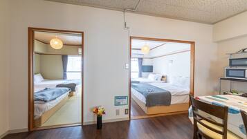 A hotel room with a wooden floor, a bed with a gray blanket, a desk with a chair, and a mirror reflecting the room.