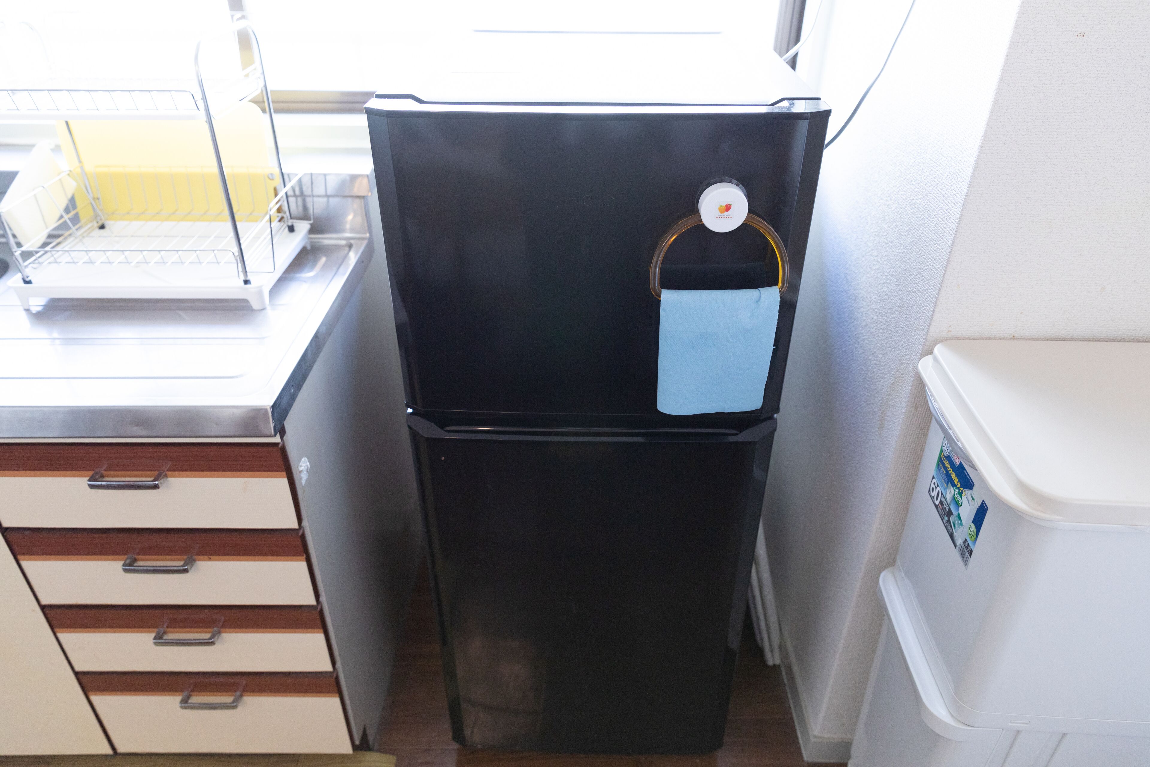 A compact kitchen with a black refrigerator, a white sink, and a small white trash bin.