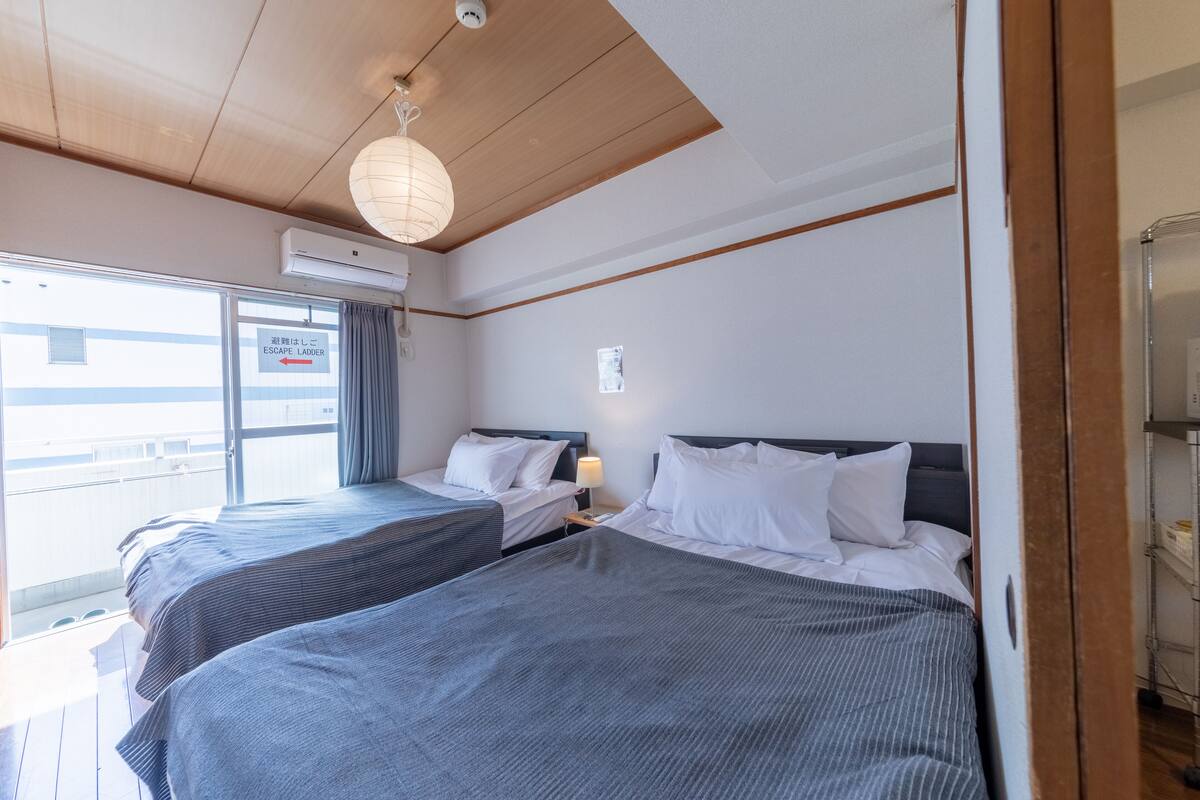 Ein Hotelzimmer mit zwei Betten, einem Vorhangfenster, einer Klimaanlage und einer Holzbalkendecke.
