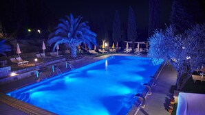 A nighttime view of a swimming pool with lounge chairs and umbrellas, surrounded by trees and a stone wall. - Casanova - Family Apartments Residence (San Quirico d'Orcia)