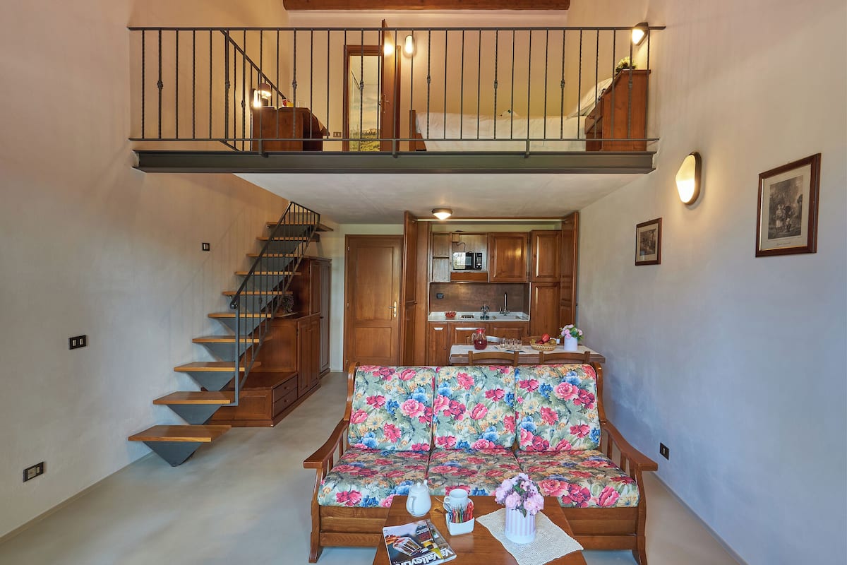 Ein geräumiger Wohnbereich mit einer Holztreppe, einem blumigen Sofa und einer Küchenzeile.