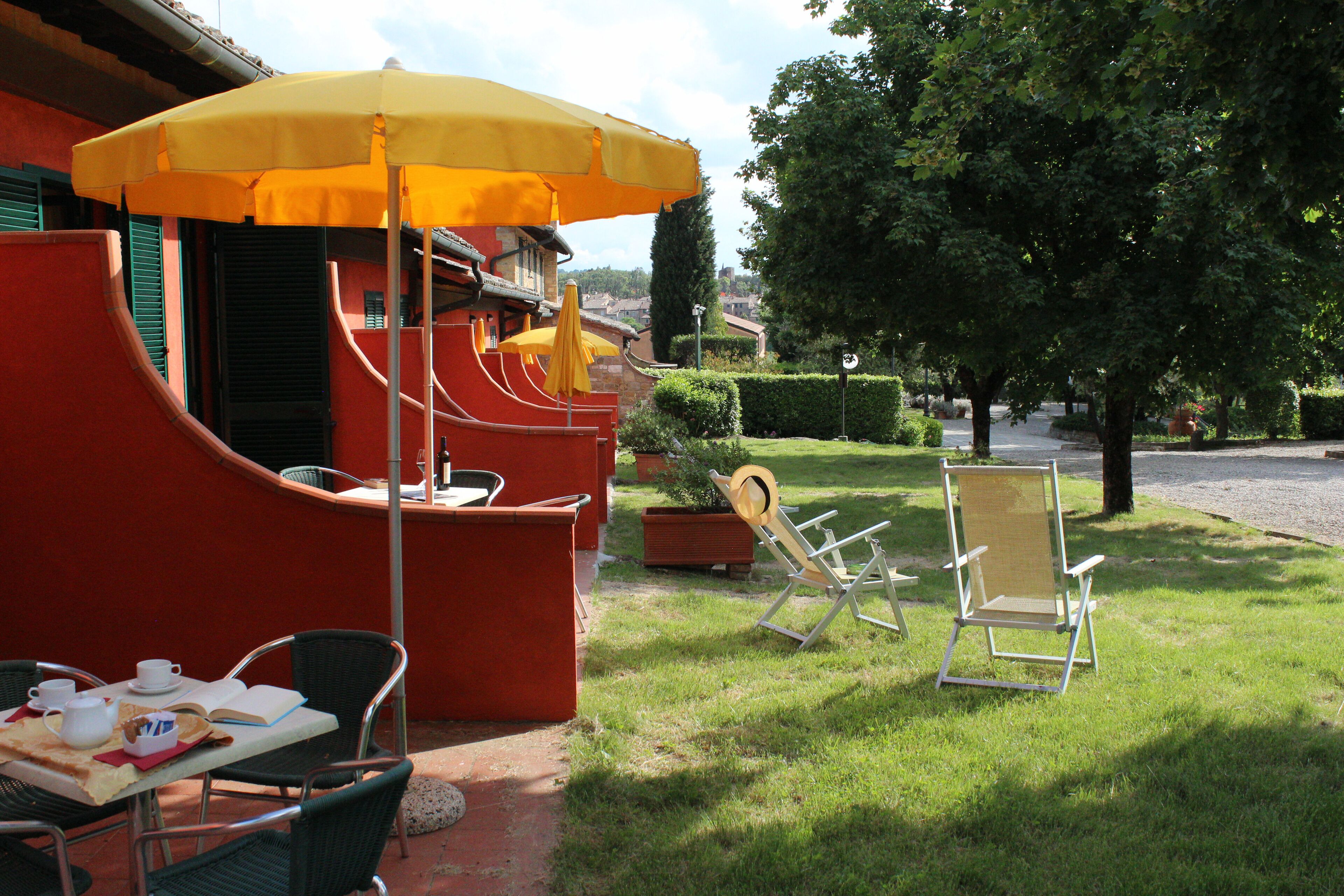 Un patio con una mesa lista para dos personas, una sombrilla amarilla y una silla.