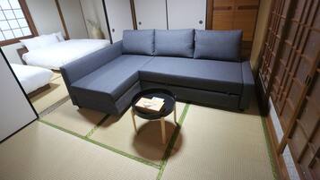 A traditional Japanese-style room with tatami flooring, a grey sofa, a small wooden table, and a white bed.