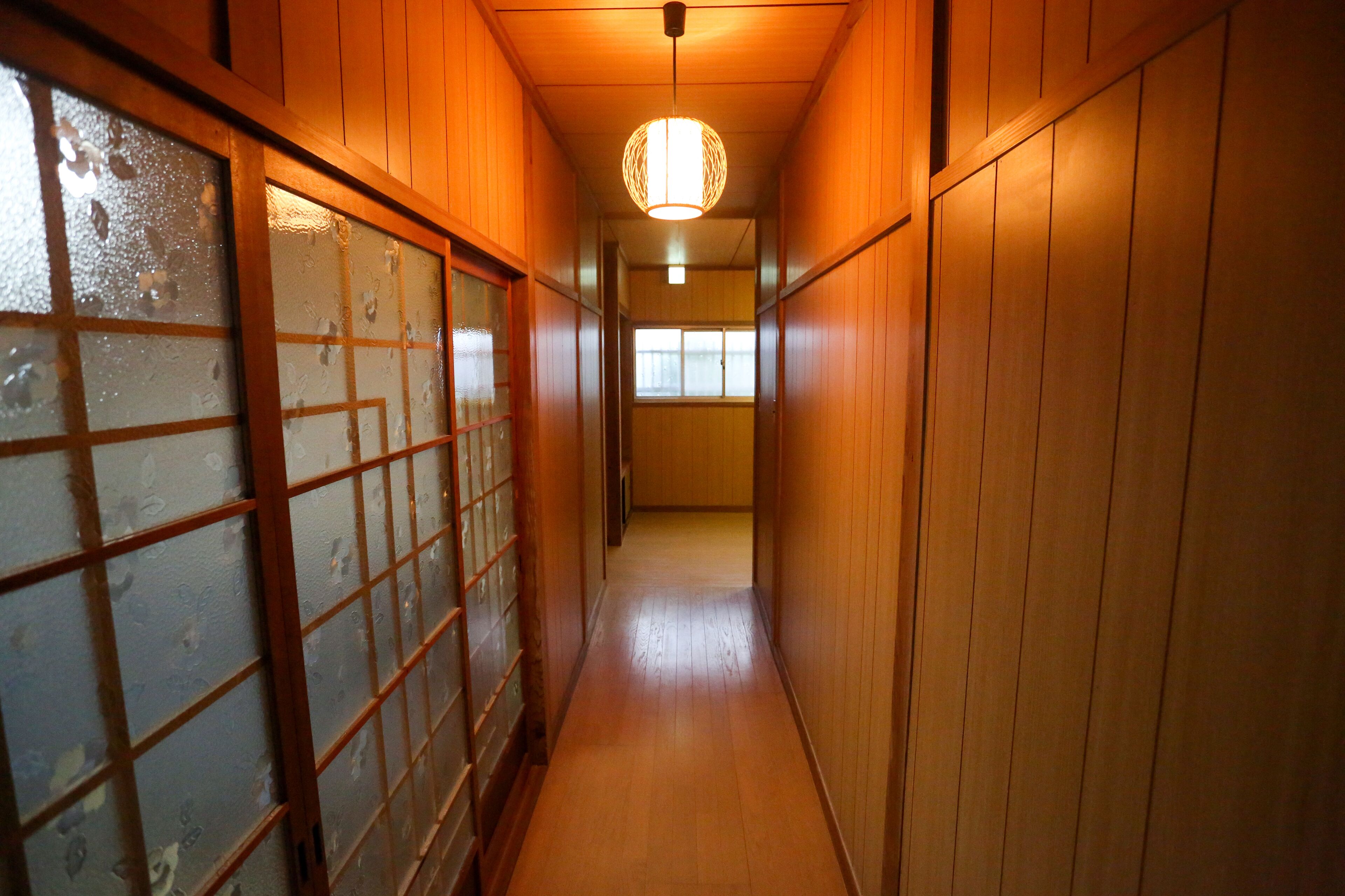A narrow hallway with wooden walls and a glass door on the left.