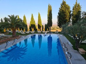A swimming pool with lounge chairs and umbrellas, surrounded by trees and a view of the landscape. - Casanova - Panoramic Rooms and Suites (San Quirico d'Orcia)
