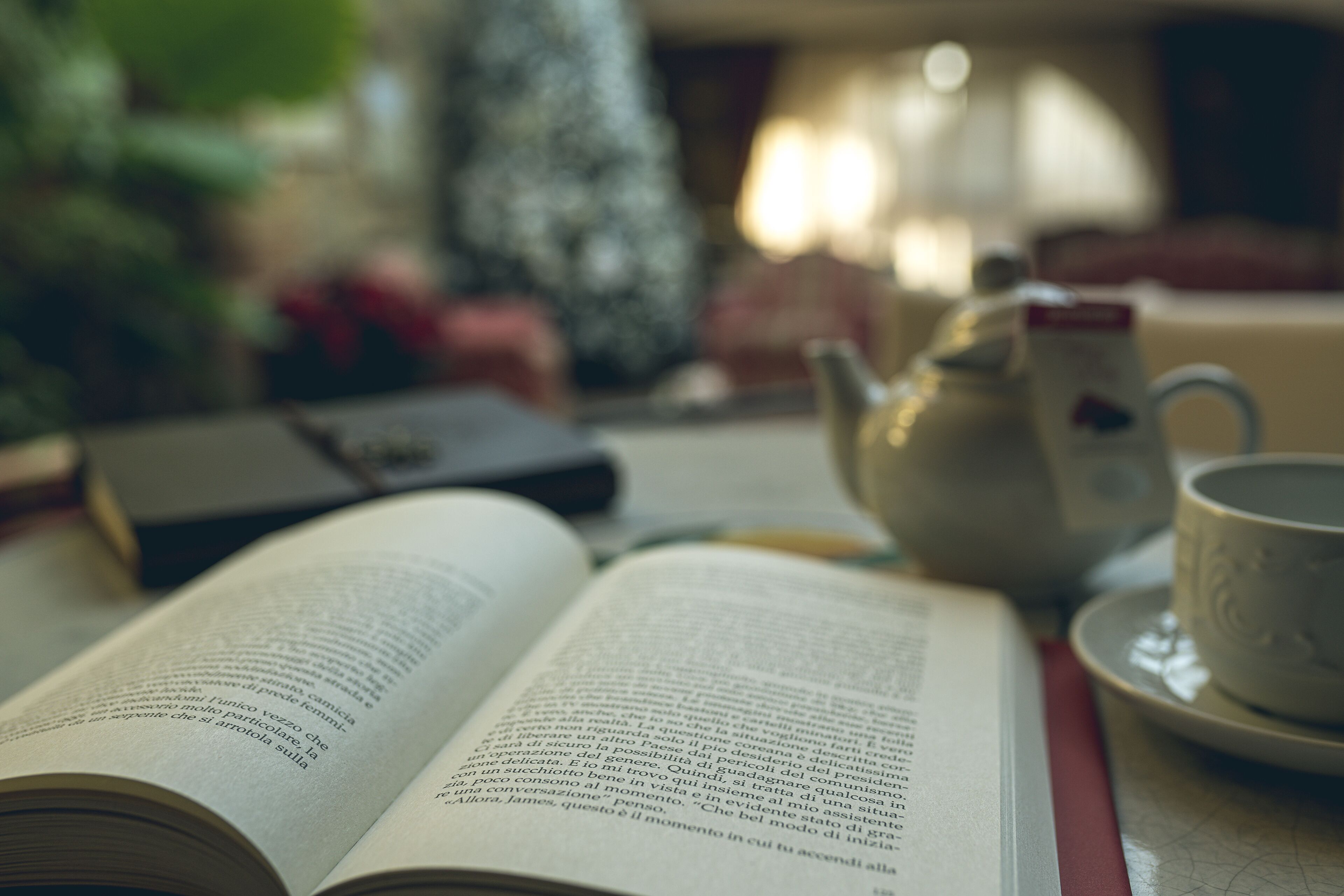 An open book on a table with a teapot and a cup.