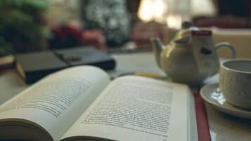 An open book on a table with a teapot and a cup.