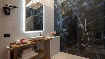 Un baño con pared de ducha de mármol, lavamanos con espejo y toallero con toallas.