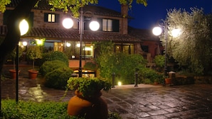 A courtyard with a stone pathway, potted plants, and a building with multiple windows and a tiled roof. - Casanova - Panoramic Rooms and Suites (San Quirico d'Orcia)