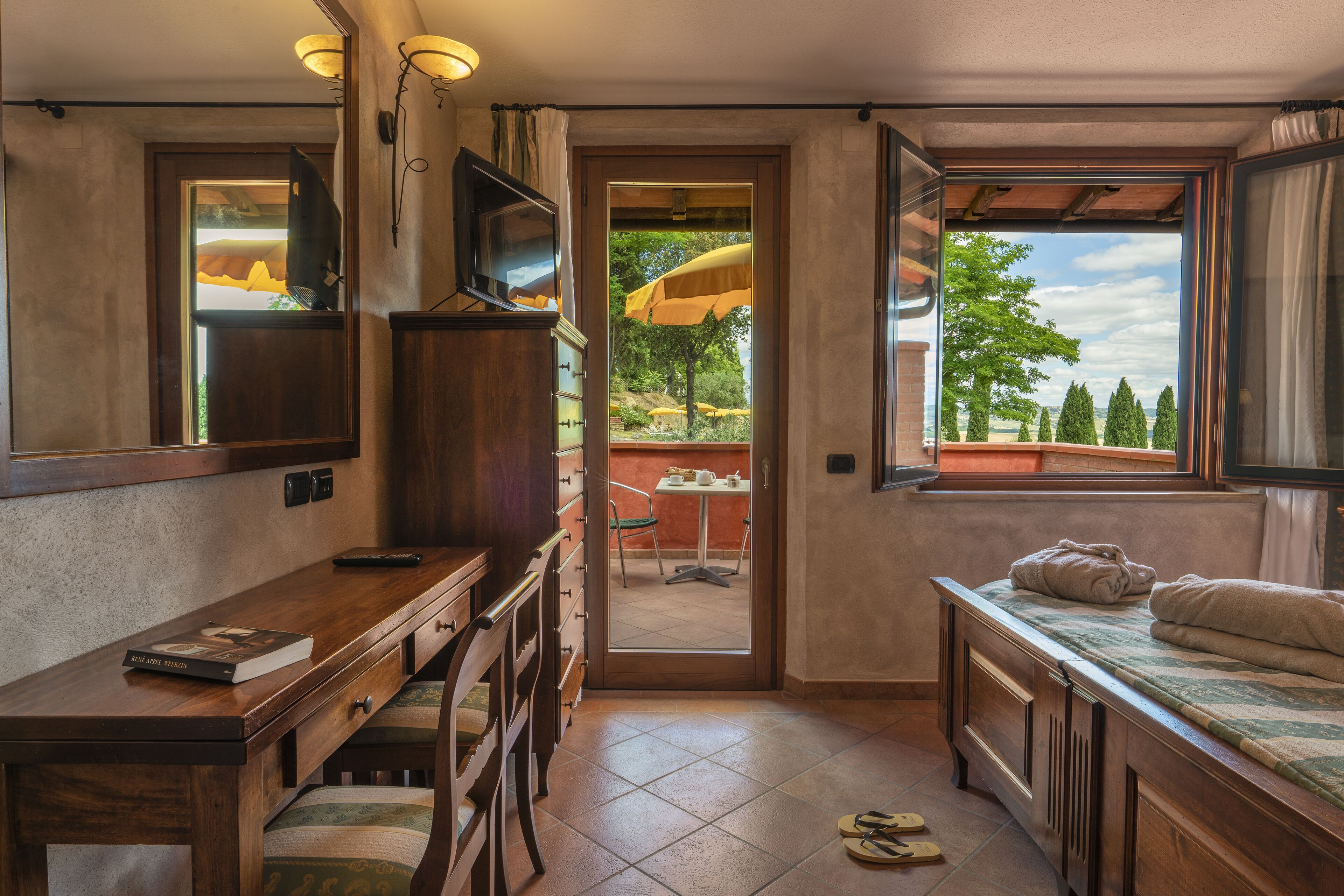 A compact room with a wooden desk, a television, and a bed with towels.