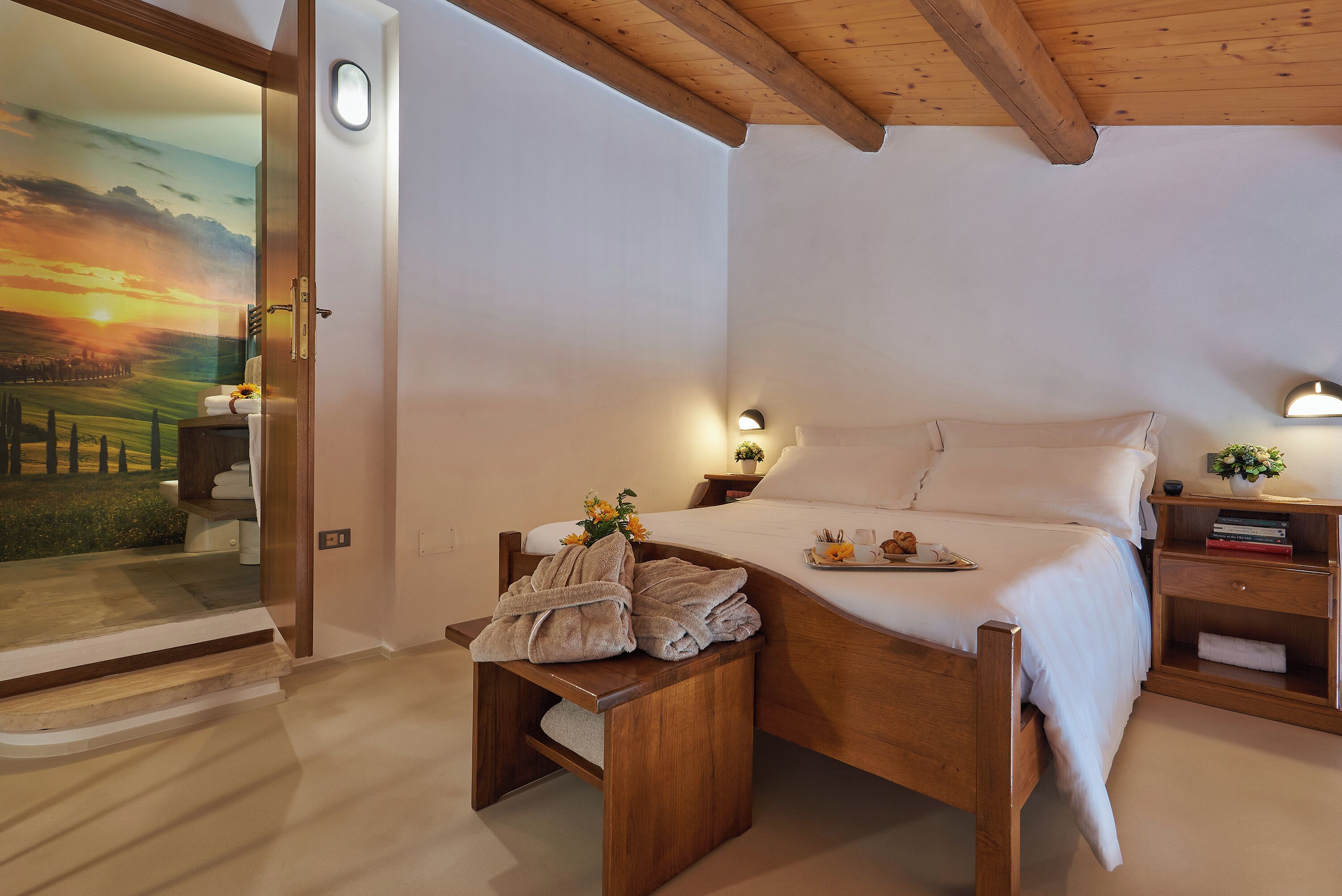 A bedroom with a wooden bed, a nightstand, a bedside table, and a view of a sunset through a glass door.
