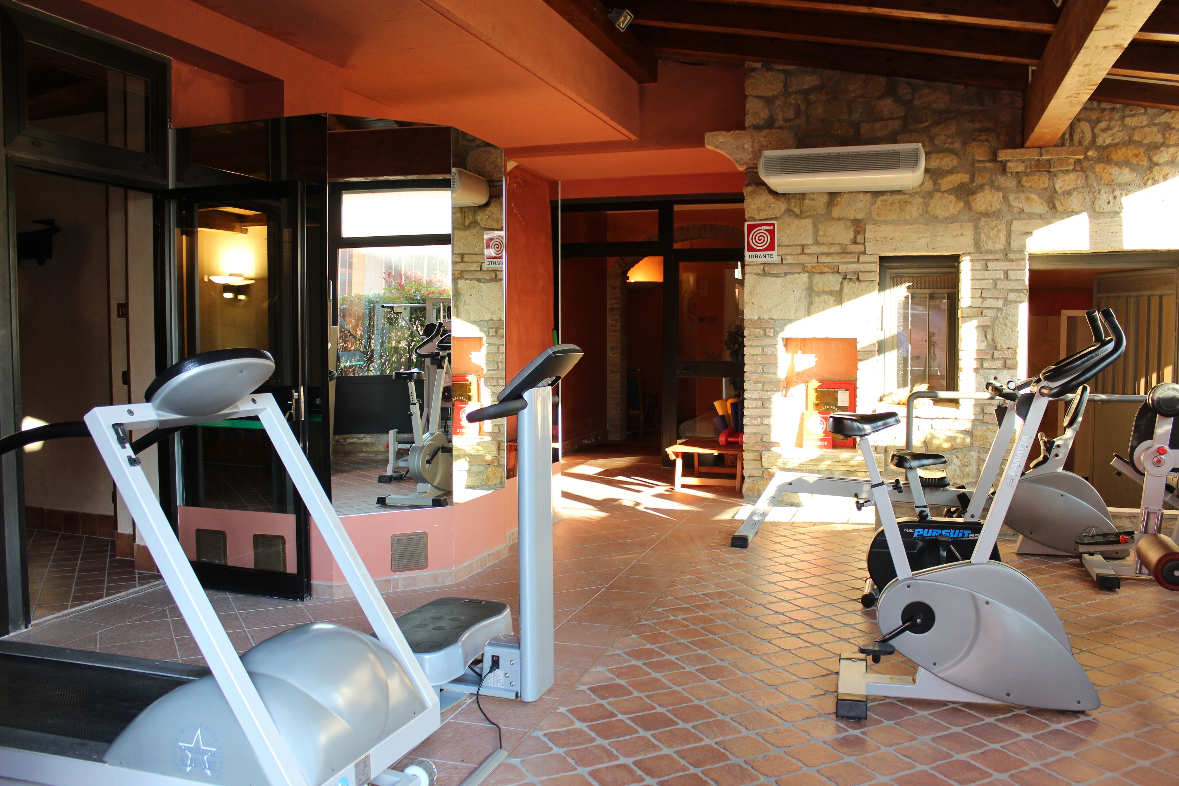 A gym with stationary bikes and treadmills, stone walls, and a tiled floor.