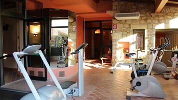 A gym with stationary bikes and treadmills, stone walls, and a tiled floor.