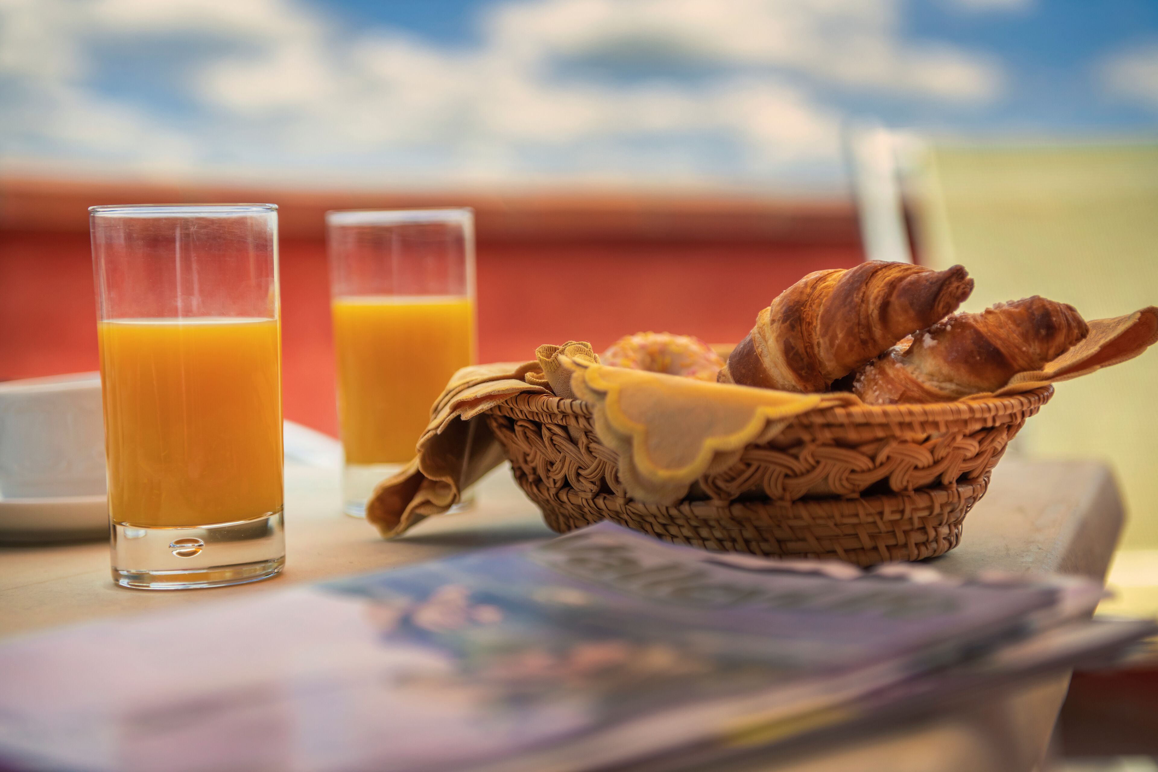 Een ontbijttafel met croissants en jus d'orange, met een heldere blauwe lucht op de achtergrond.